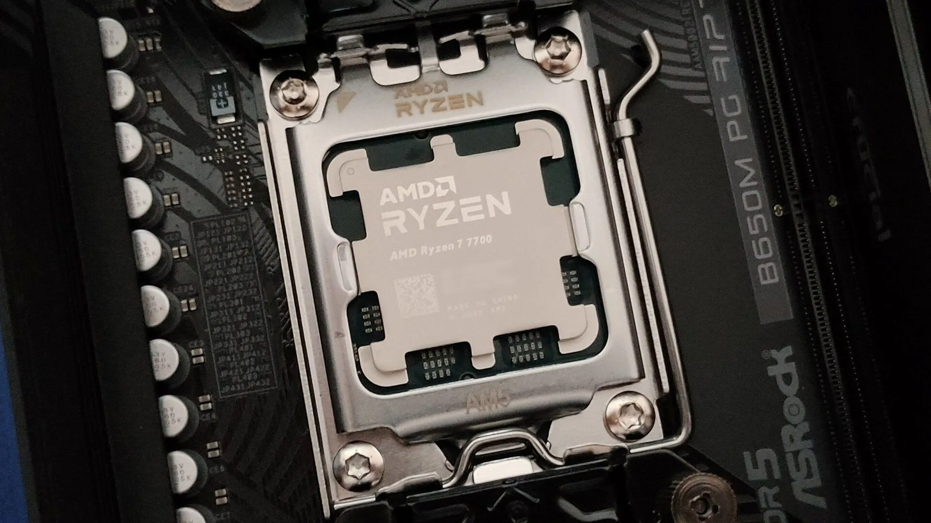 Ảnh cận cảnh CPU AMD Ryzen 7 7700 trên socket AM5 và bo mạch chủ ASRock B650M PG Riptide, minh họa linh kiện CPU.