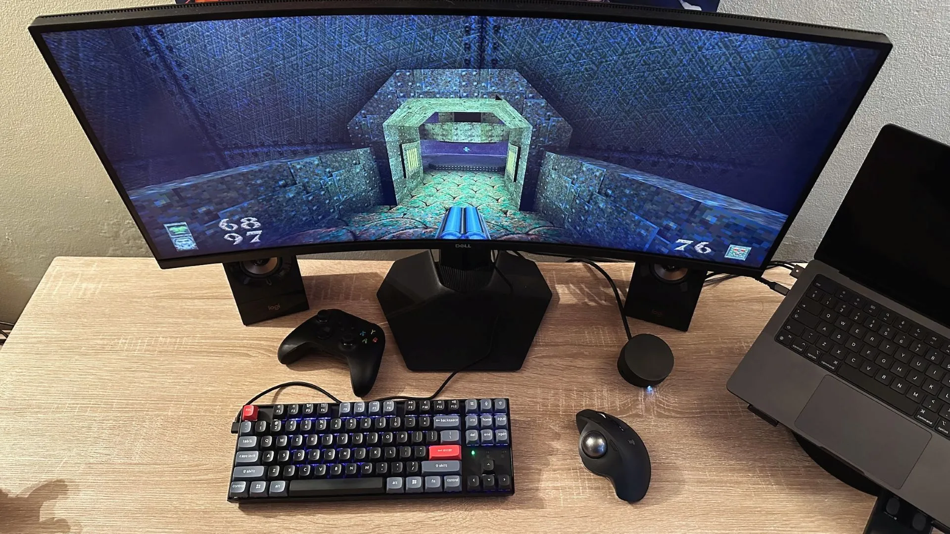 Bàn làm việc với thiết lập chơi game Quake trên màn hình và chuột bi lăn, gợi nhớ trải nghiệm chơi game cổ điển.