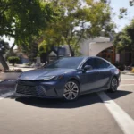 Hình ảnh Toyota Camry 2026 màu xám bạc đang di chuyển trên đường phố, làm nổi bật thiết kế đầu xe "hammerhead" và hệ dẫn động AWD điện tử mới.