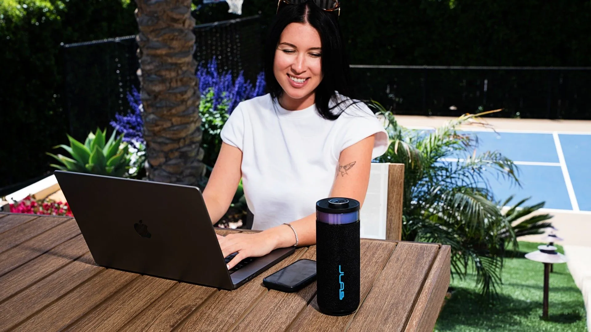 Loa JLab Go Party Speaker trên bàn làm việc cùng một người phụ nữ đang sử dụng máy tính.
