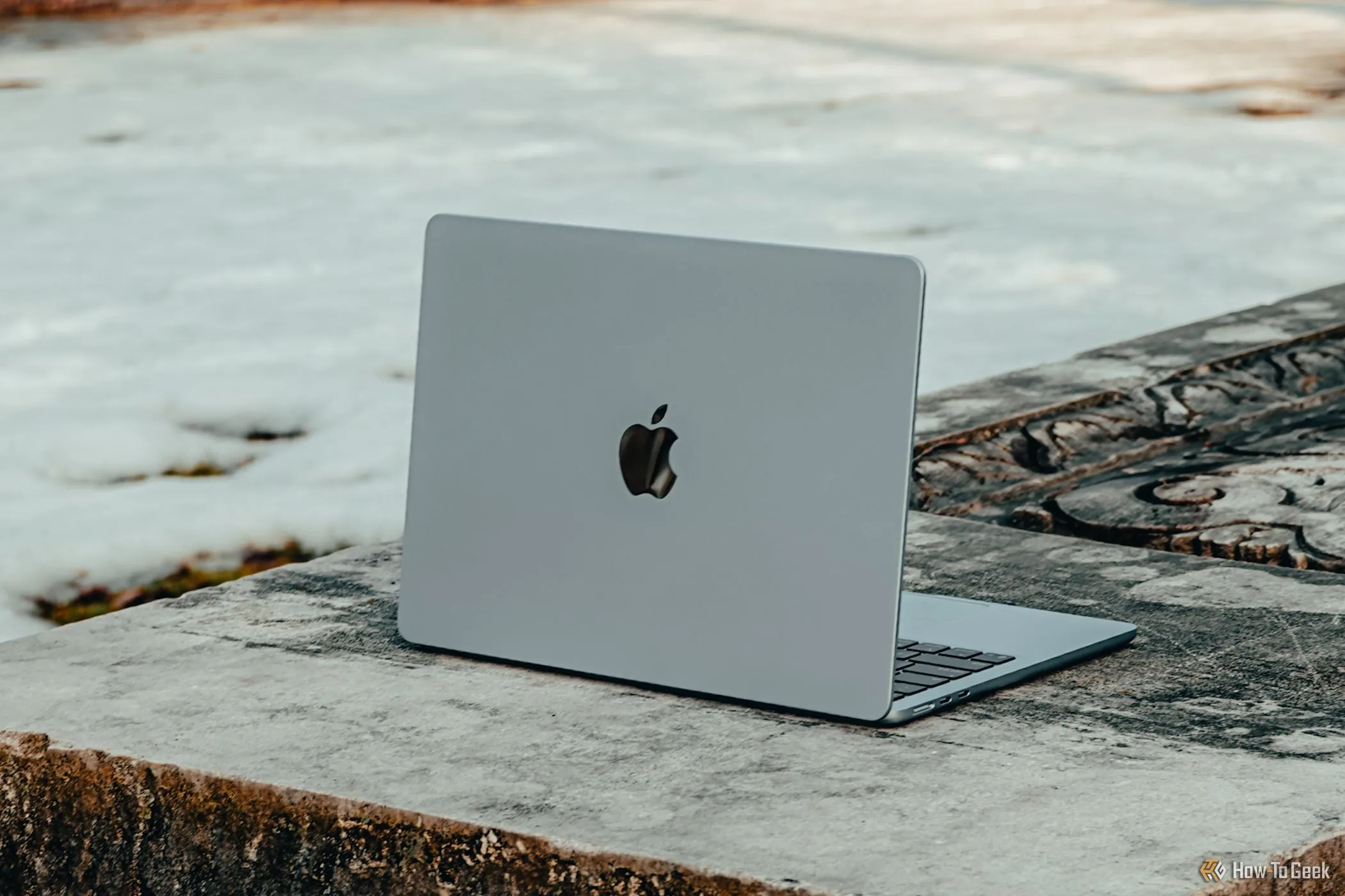 Mẫu MacBook Air M4 màu xanh lam đặt trên ghế bê tông, thể hiện thiết kế mỏng nhẹ của laptop Apple.