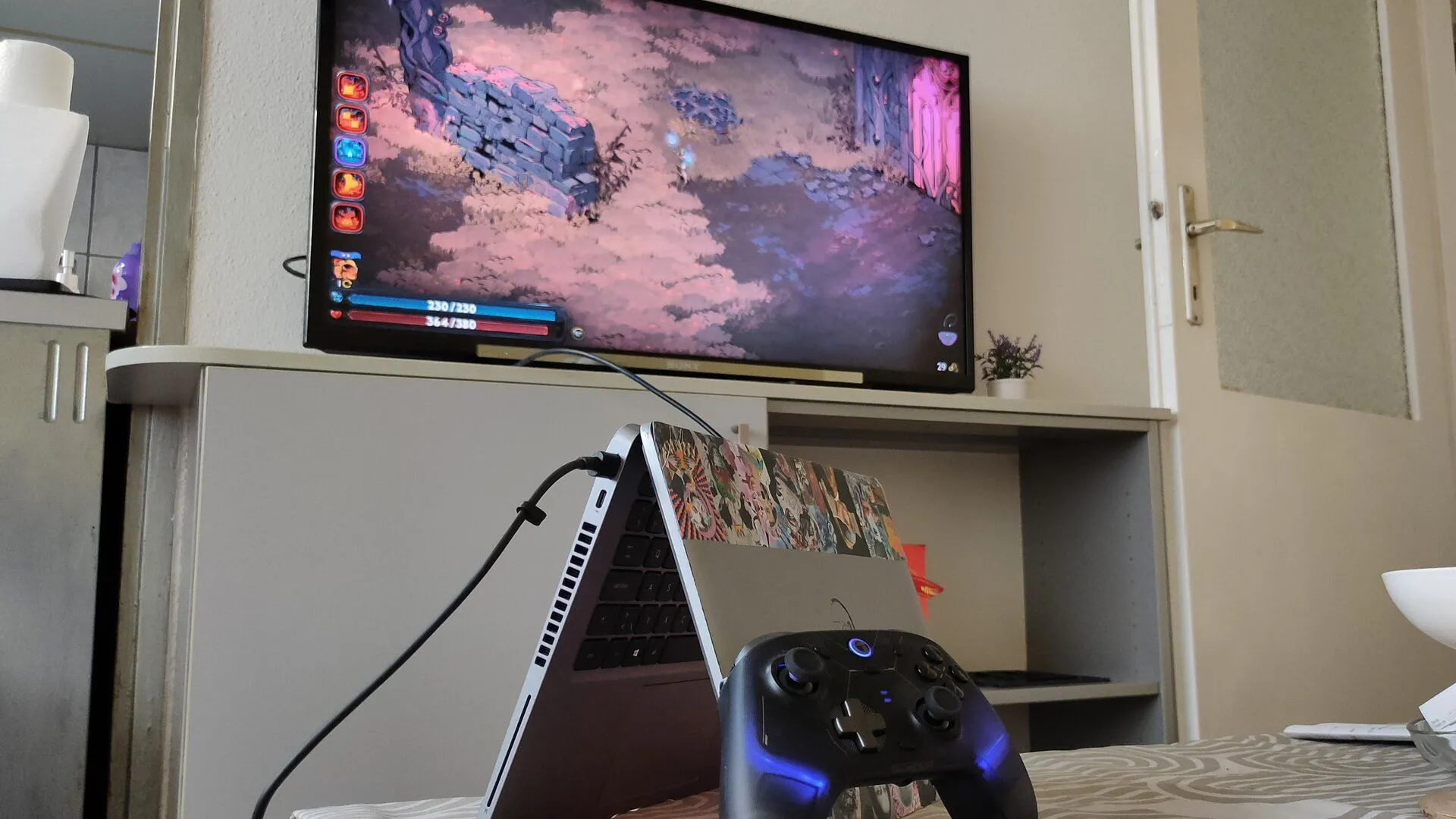 Một chiếc laptop Dell được đặt dựng nghiêng, kết nối với bộ điều khiển game và TV