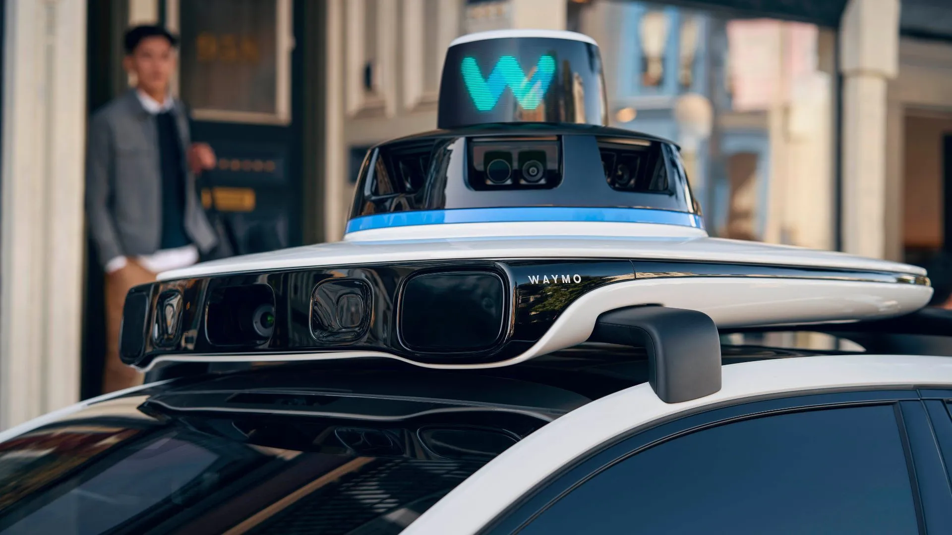 Một chiếc xe robotaxi Waymo Jaguar I-Pace với nhiều cảm biến trên nóc, đang di chuyển trên đường phố