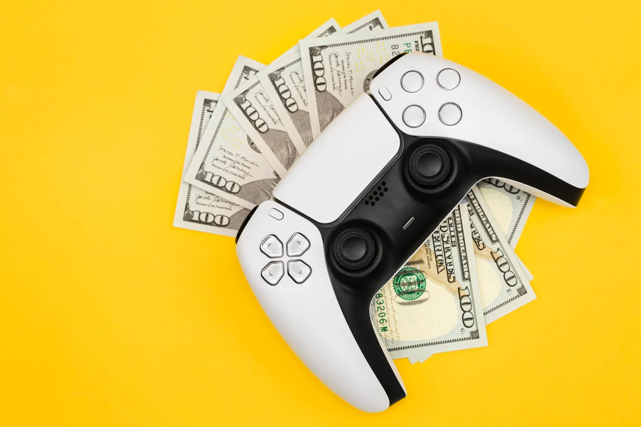 Năm tờ tiền 100 đô la dưới tay cầm PlayStation 5, tượng trưng cho chi phí phát triển game AAA và giá game ngày càng tăng cao