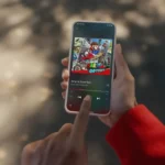 Người dùng sử dụng điện thoại iPhone để nghe nhạc trên ứng dụng Nintendo Music, hiển thị bài hát "Jump Up, Super Star" từ game Super Mario Odyssey.