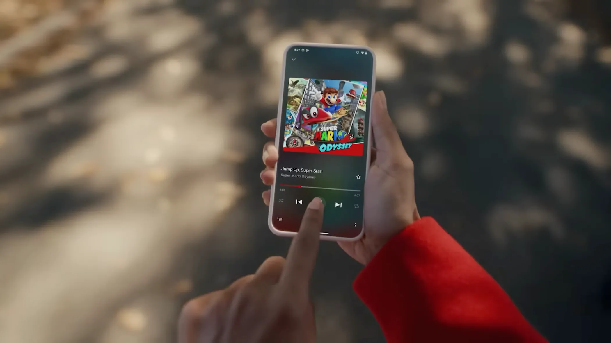Người dùng sử dụng điện thoại iPhone để nghe nhạc trên ứng dụng Nintendo Music, hiển thị bài hát "Jump Up, Super Star" từ game Super Mario Odyssey.